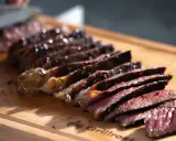 Saftiges Steak, auf einer Plancha zubereitet, wird auf einem Holzbrett in Scheiben geschnitten.