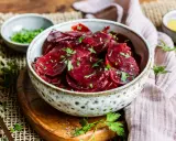 Schüssel mit traditionellem Rote Bete Salat, garniert mit Petersilie. Daneben kleine Schälchen mit Kräutern und Dressing.