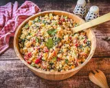 Ein bunter Couscous-Salat mediterran mit Tomaten, Gurken, Paprika und Oliven in einer Holzschüssel, bereit zum Servieren.