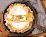 Herzhaftes Tartiflette-Rezept in Gusseisenpfanne: Kartoffeln, Speck und geschmolzener Käse, garniert mit Petersilie.