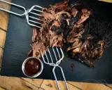 Saftiges pulled beef mit dunkler Kruste, serviert mit BBQ-Sauce.
