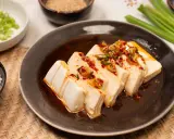 Seidiger Tofu, ein einfaches silken tofu recipe, serviert mit Frühlingszwiebeln und Chili-Öl auf einem dunklen Teller.