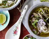 Ein dampfendes Pho-Rezept mit zarten Rindfleischscheiben, Reisnudeln, Sojasprossen und frischem Koriander in einer aromatischen Brühe. Dazu Limettenspalten.