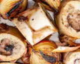 Rinderknochen auskochen Rezept: Geröstete Rinderknochen und Zwiebeln auf einem Blech, bereit für eine herzhafte Brühe.