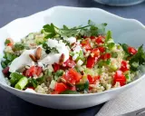 Frischer Quinoa-Salat mit Feta, Tomaten, Gurken und Kräutern, garniert mit Joghurt und Pinienkernen.