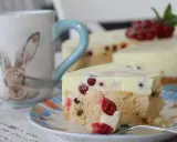 Ein Stück Johannisbeertorte mit Joghurt, dekoriert mit frischen roten Johannisbeeren. Daneben eine Tasse mit Hasenmotiv.