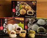 Verschiedene Sorten japanischer Reiskuchen (Mochi) mit Sesam, roter Bohne und grünem Tee, auf dunklem Untergrund vor Holz.