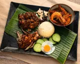 Nasi Lemak: Reis, scharfe Garnelen, frittierte Sardellen, Spiegelei, Gurkenscheiben, Cashewkerne und Rosinen auf Bananenblatt.