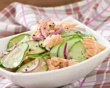 Frischer Gurkensalat mit zarten Lachsstücken und roten Zwiebelringen, gewürzt mit Pfeffer. Ein leichter und gesunder Salat.
