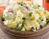 Herzhafter Kartoffelsalat mit Meerrettich, verfeinert mit Frühlingszwiebeln und roten Zwiebelringen, serviert in einer Holzschale.