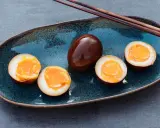 Dunkelbraune, marinierte Ramen-Eier auf einem blauen Teller, drei davon halbiert, mit flüssigem Eigelb.