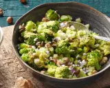 Ein einfacher Brokkoli-Salat mit Nüssen und Rosinen, serviert in einer Schüssel auf einem Holztisch.