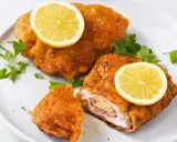 Zwei goldbraune Cordon Bleu mit geschmolzenem Käse und Schinken, garniert mit Zitronenscheiben und Petersilie.