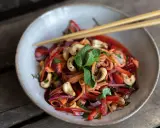 Bunter Papaya-Salat mit reifer Papaya, Karottenstreifen, Cashewkernen und Minze, serviert mit Stäbchen.