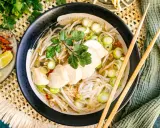 Eine dampfende Schüssel Pho Ga mit zarten Hühnerbrustscheiben, Reisnudeln, Sojasprossen und Frühlingszwiebeln. Serviert mit Limettenspalten und Chili.