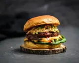 Ein saftiger koreanischer Burger mit doppeltem Patty, Käse, knackigem Krautsalat und Frühlingszwiebeln auf einem rustikalen Holzbrett.