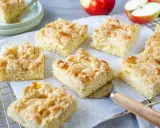 Saftige Stücke vom besten Apfelkuchen mit Streusel, frisch gebacken und bereit zum Genießen. Äpfel liegen daneben.