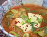 Heißes, würziges Sundubu Jjigae mit weichem Tofu, Kimchi und Frühlingszwiebeln in einer bunten Schüssel.