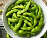 Salzige Edamame-Schoten in einer Schüssel, bereit zum Genießen. So isst man Edamame: die Schote aufbeißen und die Bohnen herausdrücken.