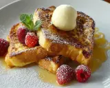 Goldbrauner Brioche French Toast mit Puderzucker, Himbeeren, Minze und einer Kugel Vanilleeis.