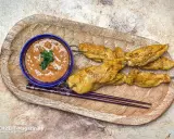 Saftige Satay Chicken Spieße mit Sesam, serviert mit Erdnusssauce und Stäbchen auf einem Holztablett.