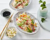 Frischer Glasnudelsalat mit knackigem Gemüse, garniert mit Sesam und Minze. Daneben Schüsselchen mit Sprossen und schwarzem Sesam.