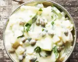 Cremiger Kartoffelsalat mit Kapern und frischen Kräutern, serviert in einer Metallschale auf rustikalem Holz.