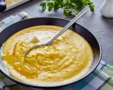 Eine Schüssel cremiger Polenta mit einem Stück Butter und einem Löffel. Was ist Polenta? Ein herzhaftes Maisgericht, das warm serviert wird.