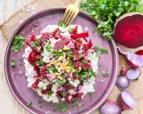 Roter Bete Salat mit cremigem Käse, Pinienkernen und frischer Petersilie auf einem lila Teller.