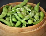 Frische Edamame-Schoten, leicht gesalzen, bereit zum rohen Essen. Ein gesunder Snack in einem Bambuskorb.