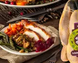 Ein festlich gedeckter Tisch mit einem Teller voller gebratenem Perlhuhn, dazu grüne Bohnen, Karotten und Cranberry-Sauce. Das unzubereitete Perlhuhn daneben zeigt das Label "Nature & Respect".