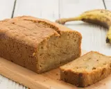 Saftiges Bananenbrot mit Skyr, frisch gebacken und auf einem Holzbrett angerichtet. Eine Banane liegt daneben.