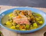 Herzhafter spanischer Eintopf mit Fleisch, Kartoffeln, Grünkohl und Karotten in einer blauen Schüssel.