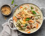 Herzhaftes Thai Curry mit Rindfleisch, zarten Möhren, grünen Bohnen und Maiskolben in cremiger Kokosmilch, garniert mit Erdnüssen und Basilikum.