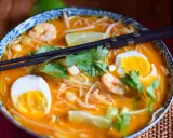 Eine Schüssel mit köstlicher Laksa Suppe, garniert mit Garnelen, Ei, Limette und Koriander.