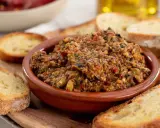 Herzhafte Tapenade deutsch in einer Tonschale, umgeben von geröstetem Brot. Ein Genuss für jeden Feinschmecker.