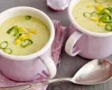 Zwei Tassen cremiger Maissuppe mit Kokosmilch, garniert mit Maiskörnern und Frühlingszwiebeln.