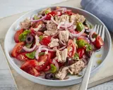 Frischer Tomaten-Thunfisch-Salat mit roten Zwiebeln und Oliven, garniert mit Basilikum. Ein leichter und gesunder Genuss.