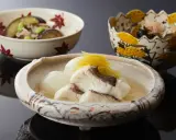Drei Schalen mit japanischem Essen. Eine Schale enthält Fisch in Brühe, was ist dashi. Eine weitere Schale mit Auberginen und Edamame.