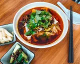 Eine Schüssel mit aromatischer taiwanischer Rindernudelsuppe, garniert mit frischem Koriander, daneben eingelegte Gurken und Rettich.