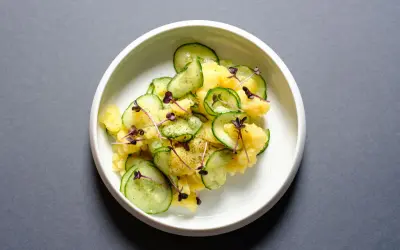 Kartoffelsalat mit frischer Gurke, garniert mit lila Sprossen und Dill. Ein leichter und erfrischender Genuss.