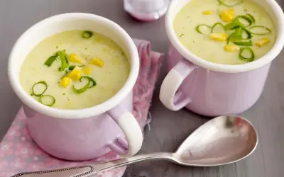 Zwei Tassen cremiger Maissuppe mit Kokosmilch, garniert mit Maiskörnern und Frühlingszwiebeln.