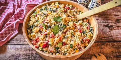 Ein bunter Couscous-Salat mediterran mit Tomaten, Gurken, Paprika und Oliven in einer Holzschüssel, bereit zum Servieren.