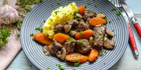 Herzhaftes Boeuf Bourguignon Rezept mit zartem Rindfleisch, Karotten, Pilzen und Kartoffelpüree, garniert mit Petersilie.