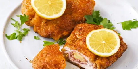 Zwei goldbraune Cordon Bleu mit geschmolzenem Käse und Schinken, garniert mit Zitronenscheiben und Petersilie.
