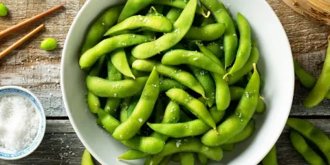 Salzige Edamame-Schoten in einer Schüssel, bereit zum Genießen. So isst man Edamame: die Schote aufbeißen und die Bohnen herausdrücken.