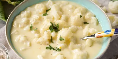 Cremige blumenkohlsuppe thermomix ohne kartoffeln, garniert mit Petersilie. Ein Löffel mit buntem Muster liegt in der Schüssel.
