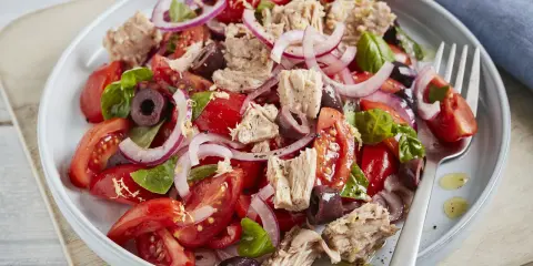 Frischer Tomaten-Thunfisch-Salat mit roten Zwiebeln und Oliven, garniert mit Basilikum. Ein leichter und gesunder Genuss.