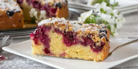 Ein saftiges Stück Streuselkuchen mit Marmelade und Puderzucker bestreut, bereit zum Genuss.