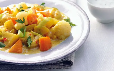 Ein Teller mit cremigem Curry-Eintopf, gefüllt mit Kartoffeln, Karotten und Lauch, garniert mit Petersilie.